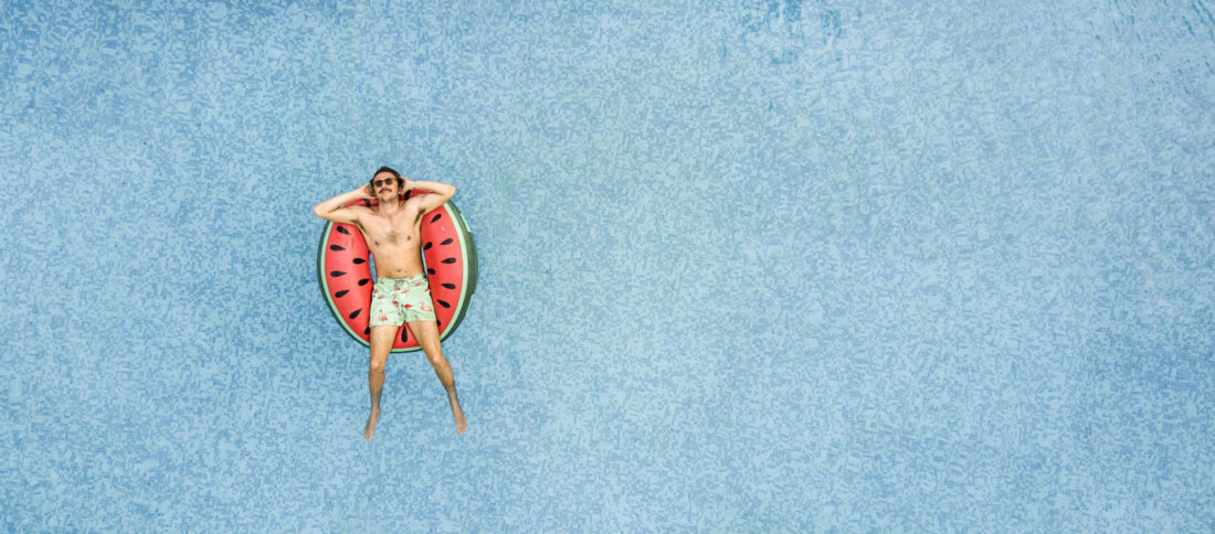 Man floating on swimming pool on a watermelon print rubber ring to promote Travel Insurance by Evalee Insurance brokers