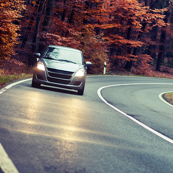 Car driving down quiet road in Autumn to promote car insurance by Evalee Insurance Brokers