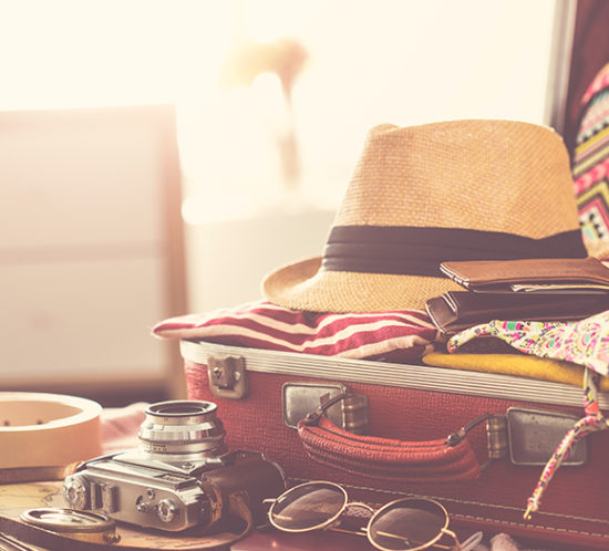 Packed suitcase laying open on bed, complete with a straw hat, camera and sunglasses to promote travel insurance by Evalee Insurance Brokers